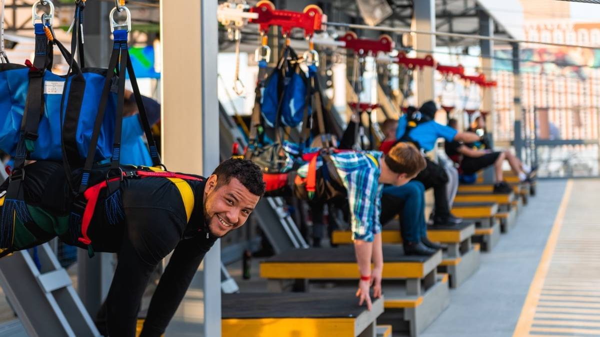 A person strapped into a zipline harness smiling at the camera with several more people lined up beside them
